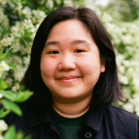 Head shot of Vivian Lee, who is wearing a dark shirt and has a gentle smile as she is photographed amidst flowering bushes