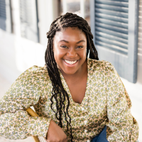 Head shot of Kayla Lightner, who sits outside on a porch in a light-colored blouse, smiling